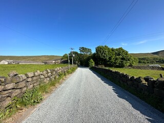 “Yorkshire countryside with a gravel road, stone walls, green fields and power lines, under a clear blue sky near Mankinholes, Todmorden, UK