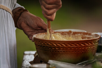 A person prepares batter in a woven bowl at an outdoor cooking setup, surrounded by rustic...