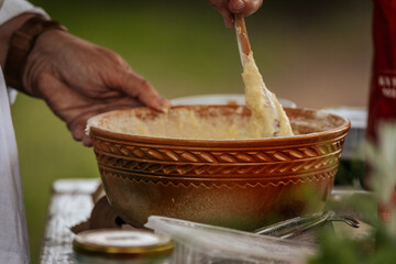 A person prepares batter in a woven bowl at an outdoor cooking setup, surrounded by rustic...