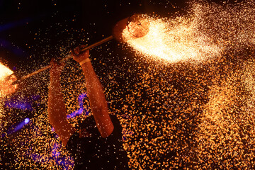 A dramatic silhouette of a fire performer wielding a flaming staff, surrounded by golden sparks in...
