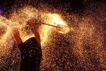 A dramatic silhouette of a fire performer wielding a flaming staff, surrounded by golden sparks in...