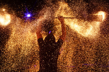 A dramatic silhouette of a fire performer wielding a flaming staff, surrounded by golden sparks in...