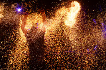A dramatic silhouette of a fire performer wielding a flaming staff, surrounded by golden sparks in a vibrant night setting.