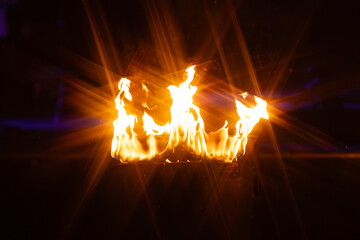 A vivid burst of orange flames rises from a metal container in the dark, captured with a starburst...