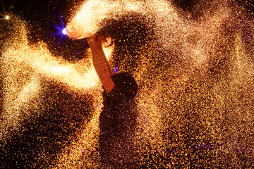 A dramatic silhouette of a fire performer wielding a flaming staff, surrounded by golden sparks in...