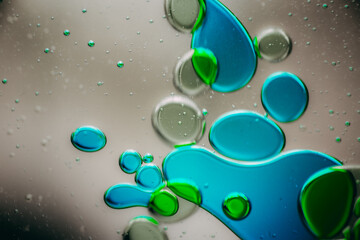 Vibrant green droplet encased in a blue fluid form, set against a neutral background with tiny...