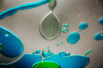Vibrant green droplet encased in a blue fluid form, set against a neutral background with tiny suspended bubbles for added texture and depth.