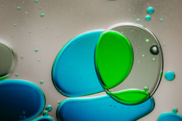 Vibrant green droplet encased in a blue fluid form, set against a neutral background with tiny...