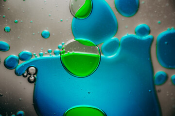 Vibrant green droplet encased in a blue fluid form, set against a neutral background with tiny...