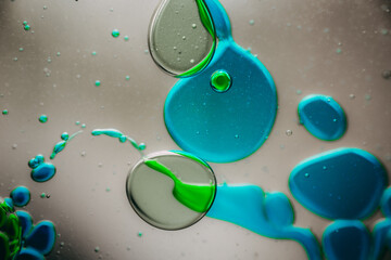 Vibrant green droplet encased in a blue fluid form, set against a neutral background with tiny...