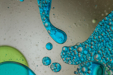 Vibrant green droplet encased in a blue fluid form, set against a neutral background with tiny...