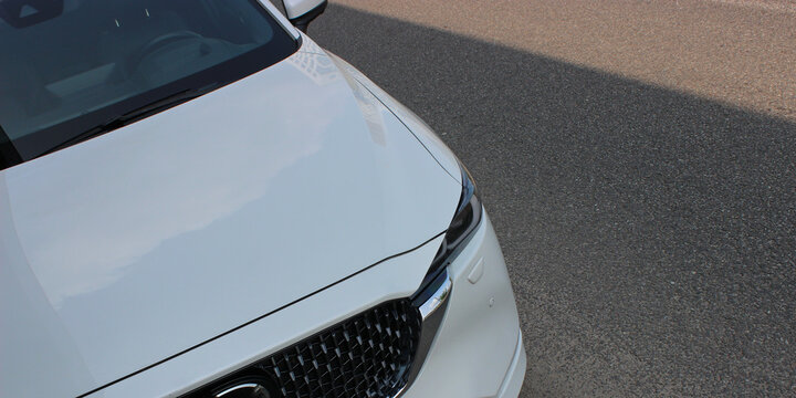 Hood and Headlight of White Car on the Asphalt at Street. Car Parked in Shade to Avoid Sun Heating 
