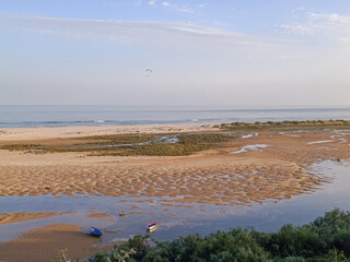Boats in the Ria Formosa at low tide at sunset and paragliding over the sea at Cacela Velha beach,...