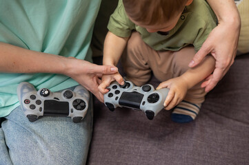 Caucasian woman teaches her little son to play console. Joystick in hands. 