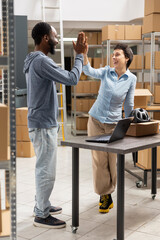 Diverse workers team in a logistics hub share a cheerful high five after completing delivery...