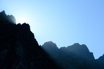  Sunset over silhouettes of high mountain ridges with sun rays coming through the mountains....