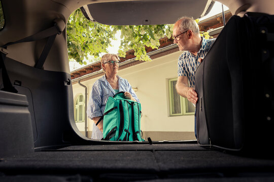 Senior couple loading their luggage in the car trunk for a vacation drive and preparing with road essentials. Retired excited people embrace the free time and comfort of travelling together.