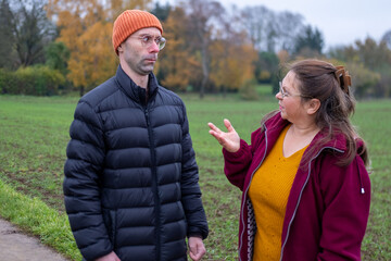 Older mother and adult son argue in autumn park, emotional distance, family conflict, generational...