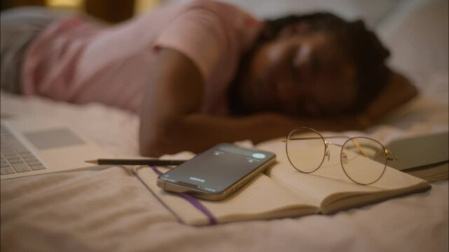 Sleeping napping African American woman female girl writer student lying down on bed sleep nap tired study calling mobile phone on book no sound don't hear call smartphone at home bedroom late night