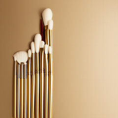 A set of gold-handled makeup brushes arranged in a diagonal pattern against a beige background.
