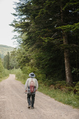 Fisherman walking on dirt road in forest, carrying fishing rod and net