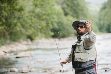 Fisherman casting line in river, trout fishing in mountain stream