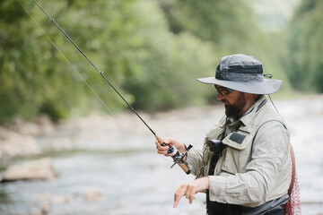 Fisherman reeling in line while fly fishing in river