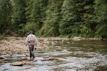 Fisherman walking in river searching for trout during summer day