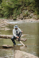 Fisherman tying shoelaces sitting on a log in the river while trout fishing