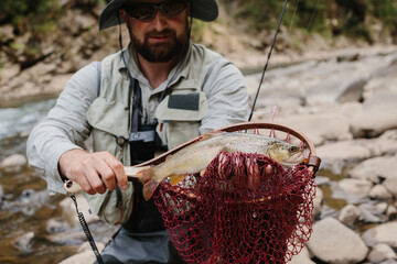 Fisherman holding brown trout in landing net in river