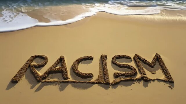 Word racism written in sand as ocean water approaches.
