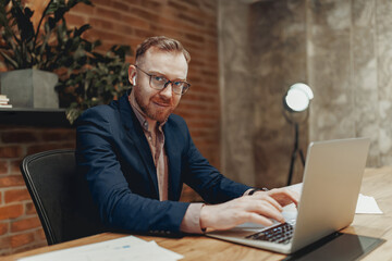 A man dressed in a tailored suit diligently working on a laptop within a contemporary office...