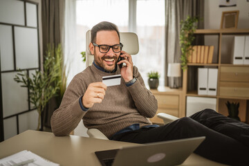 Adult businessman talk on mobile phone and hold credit card at office