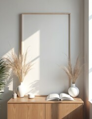 Minimalist interior mock-up featuring blank canvas on light wall with natural light. Wooden cabinet holds vases with dried pampas grass, small bowl, and open book, creating cozy and stylish ambiance.