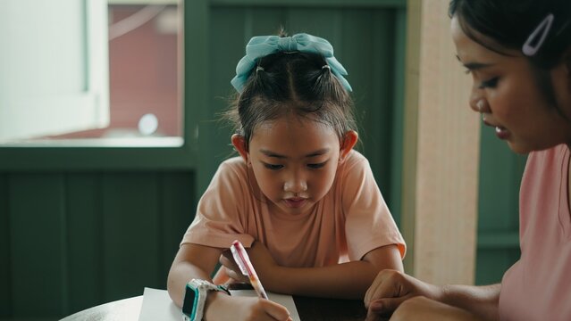 Young girl writing with adult assistance at a table