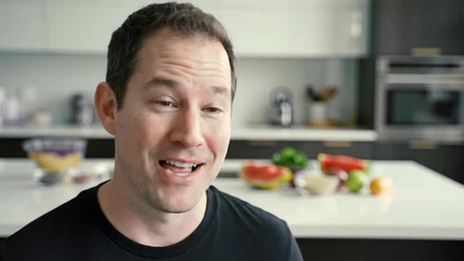 Smiling man in modern kitchen talking about healthy lifestyle and nutrition with fresh fruits and vegetables in background. Concept of wellness advice, food blogger, clean eating tips