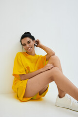 smiling woman in yellow casual outfit sitting on floor against white background, youthful, relaxed,...