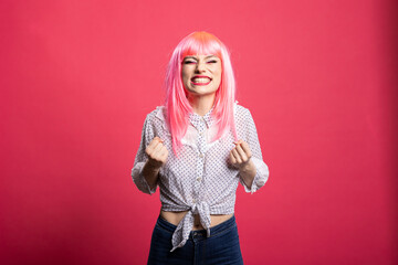 Gorgeous woman in pink hair feeling extremely excited, celebrating a win with her raised fists and...