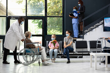 Little girl offering flowers during visiting hours with grandma in wheelchair, offer bouquet and...