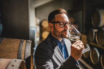Adult man winemaker hold glass stand between the barrels in cellar