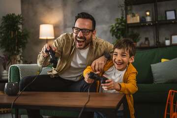 Father and son play video games with joystick and have fun at home