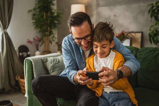 Father and son play video games on a mobile phone and enjoy at home