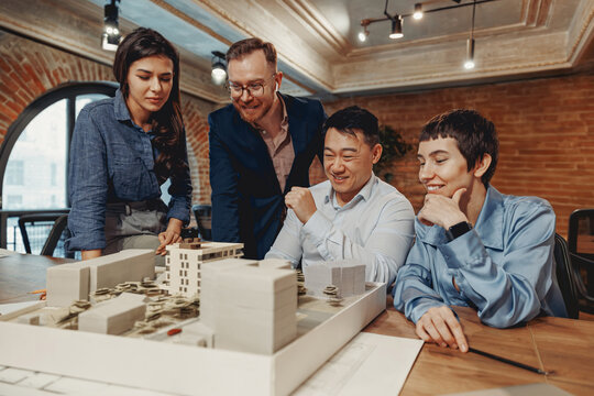 A diverse group of professionals collaborating on an architectural model, showcasing teamwork and creativity.