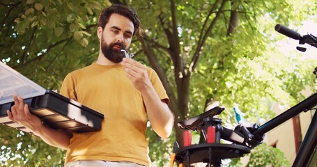 Young male cyclist prepares for bicycle maintenance by sorting different specialized work tools on...