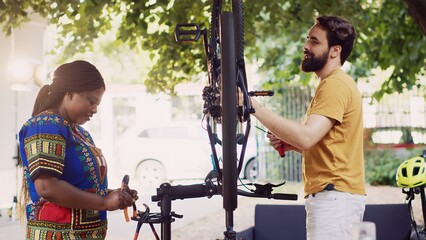 Energetic sporty interracial couple grabbing various specialized equipment from toolbox for bicycle repair in home yard. Young black woman helping man prepare expert tools for bike maintenance.