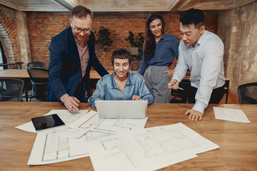 A diverse team collaborates on an innovative project in a modern office with plans and advanced...
