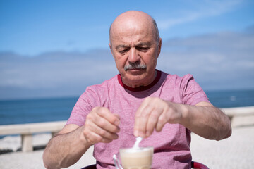 Elderly Man Adding a Lot of Sugar to Coffee While Sitting on a Summer Terrace