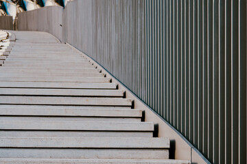 Curved concrete steps leading up to a modern building surrounded by a sleek, metallic railing in an...