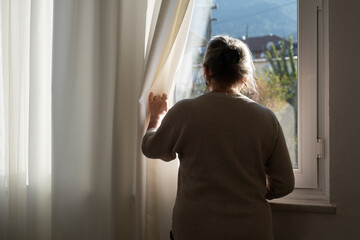 Lonely Elderly Woman Standing by the Window Looking Outside Waiting for a Visitor