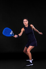 Young female athlete playing padel in dark neon studio light showing powerful movement energy and...